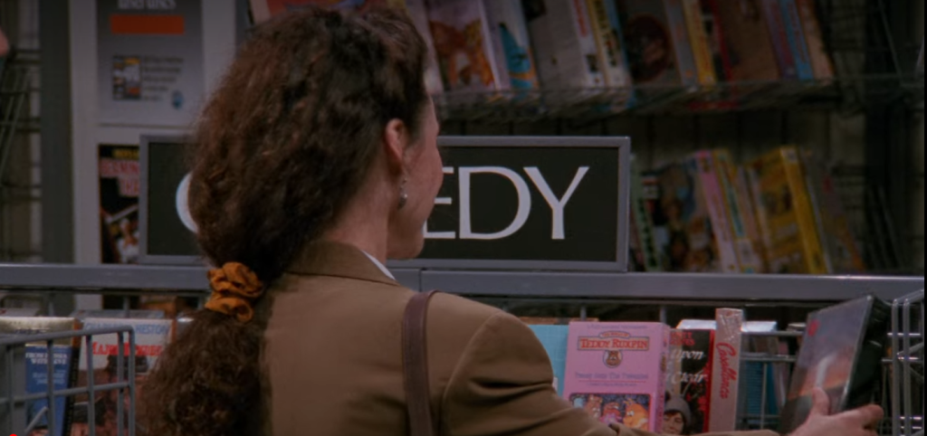 A screenshot from Seinfeld of Elaine picking a video off a shelf in a video rental store.