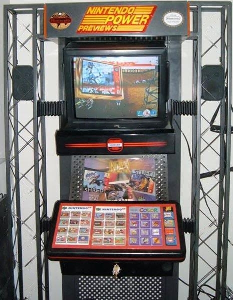 photo of a nintendo power previews kiosk. There's a TV screen playing a game commercial, and underneath is a panel with a series of buttons that have pictures of game boxes on them.