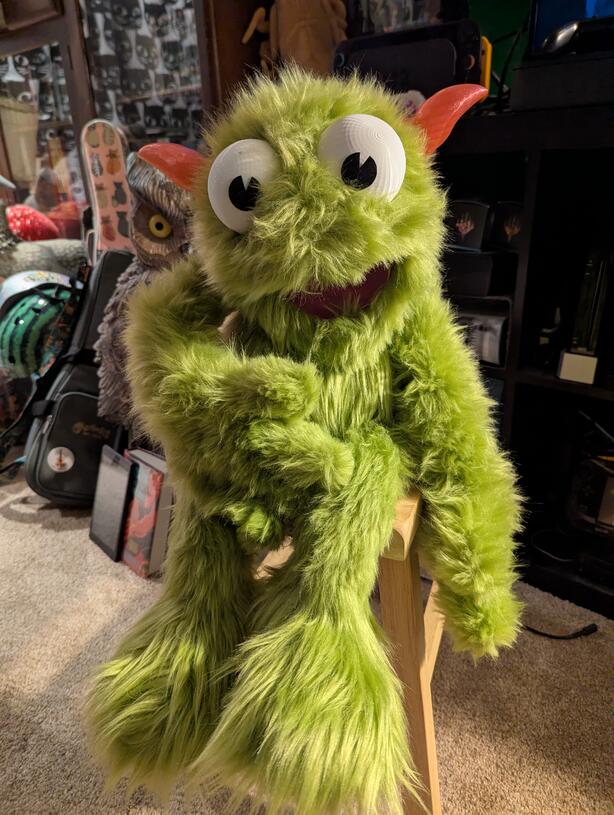 a green puppet with big eyes and pink horns